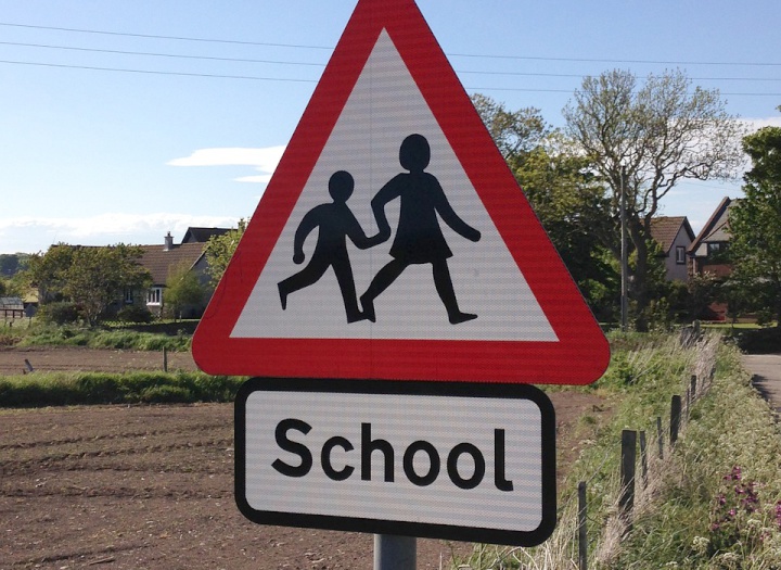 a road sign for a
school zone in a town beside a field