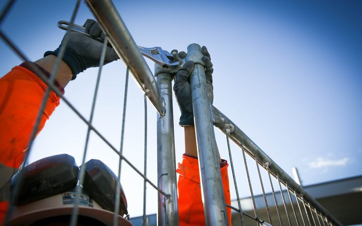 the arms of a
worker in high viz gear tightening a bolt on a steel fence