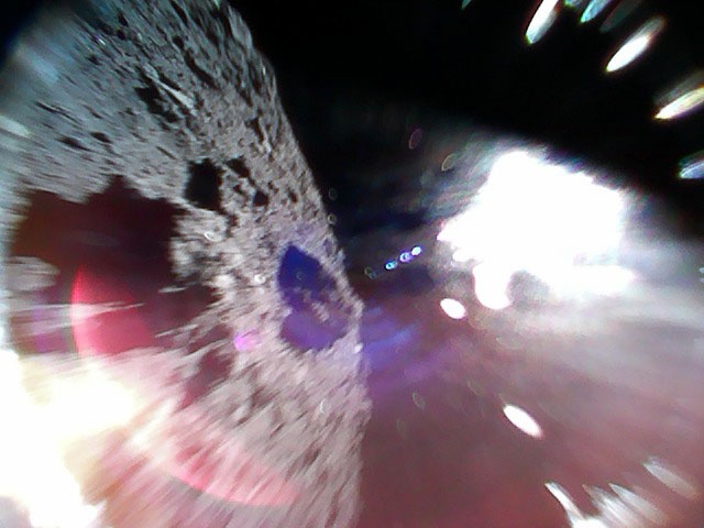 Figure 3: Image
captured by Rover-1A on September 22 at around 11:44 JST.
Color image captured while moving (during a hop) on the
surface of Ryugu. The left-half of the image is the asteroid
surface. The bright white region is due to sunlight. (Image
credit: JAXA). 