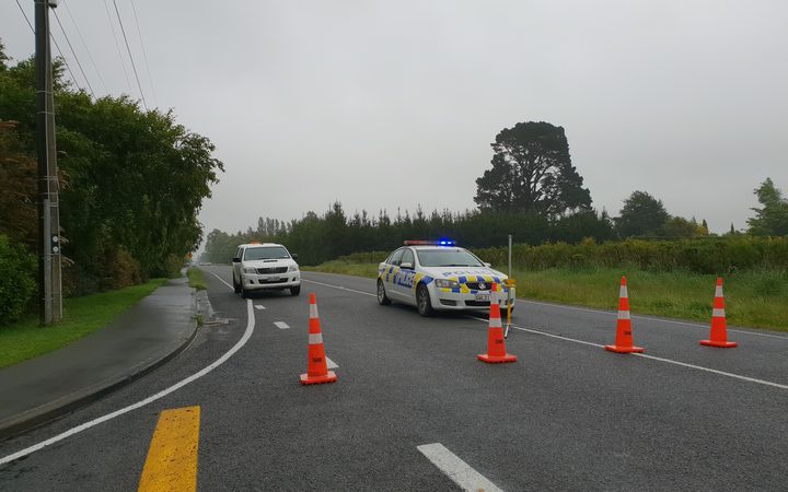 rural road, one
lane blocked by traffic cones, with police cars