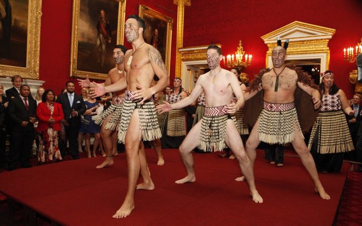 traditionally-dressed haka performers on a platform
stage in a sumptuous room