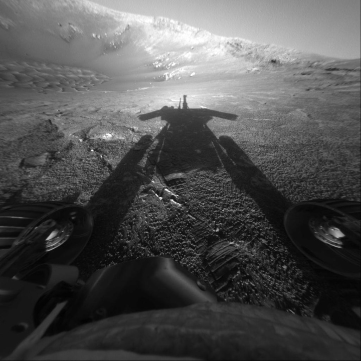 the long shadow of
the rover cast across a dimpled sandy-looking landscape
looking across a crater