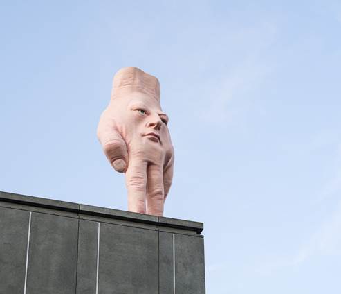 on a rooftop, a large statue of a hand standing upright on its fingers, with a human face on its back