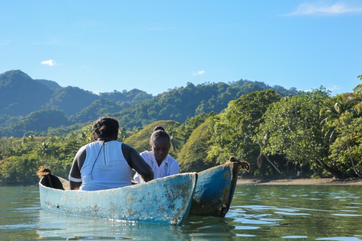 two women in a
small double-hulled boat off forested land