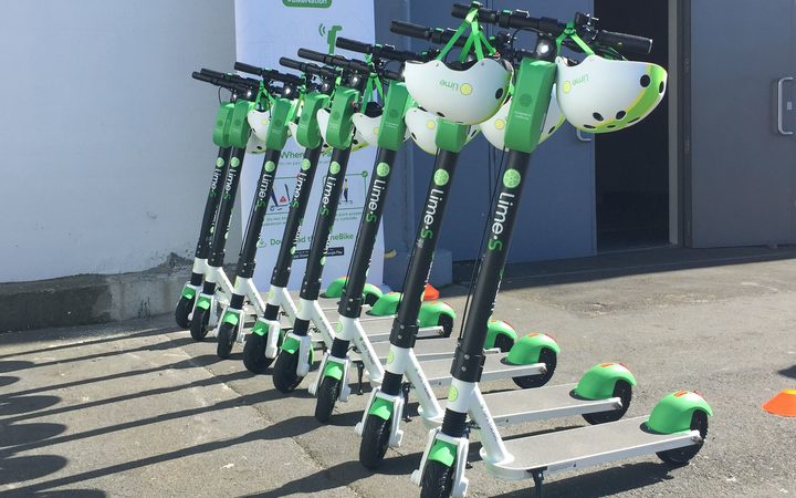 a row of lime
scooters, with helmets hanging from the handlebars