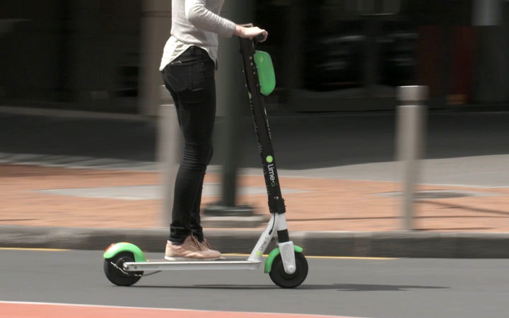 a person riding a
lime scooter on a road, with background blur suggesting
speed
