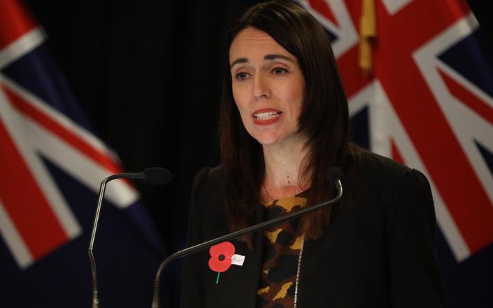 Jacinda Ardern at
the press conference, wearing an Anzac oppy with flags in
the background