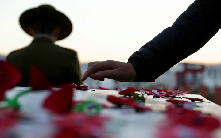a hand over ANZAC
poppies placed on the tomb of the unknown soldier, with a
soldier visible behind