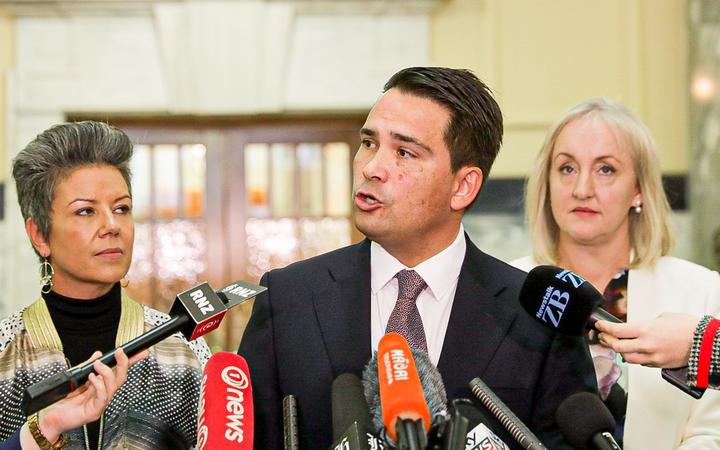 Simon Bridges
speaks into media microphones at Parliament, flanked by
Paula Bennett and Amy Adams