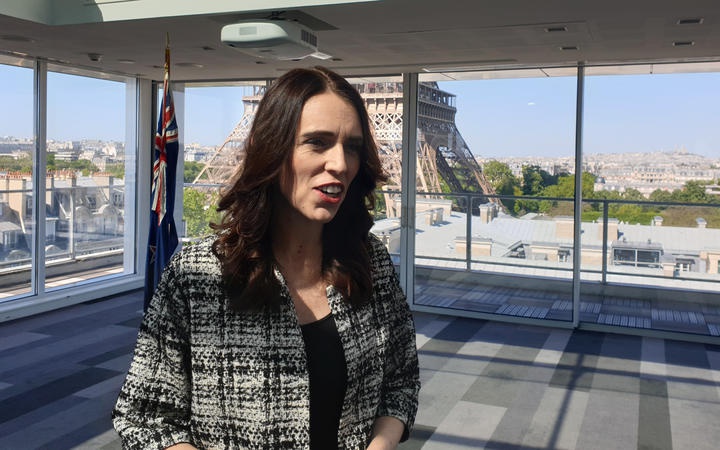 Jacinda Ardern in a
open-space room. The Eiffel Tower is visible nearby through
the floor-to-ceiling windows