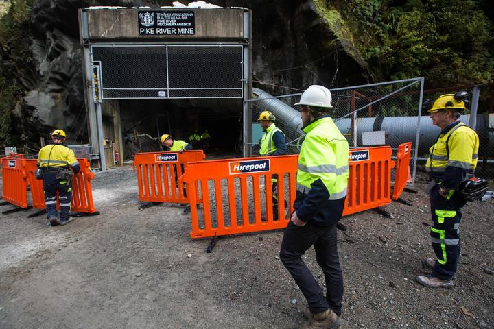 people in high viz
clothing and hard hats placing a plastic barrier fence
outside the mine entrance