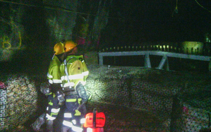 two people in
firwefighter-looking high viz clothing and hard hats in a
dimly lit tunnel space with various constructed barriers
visible