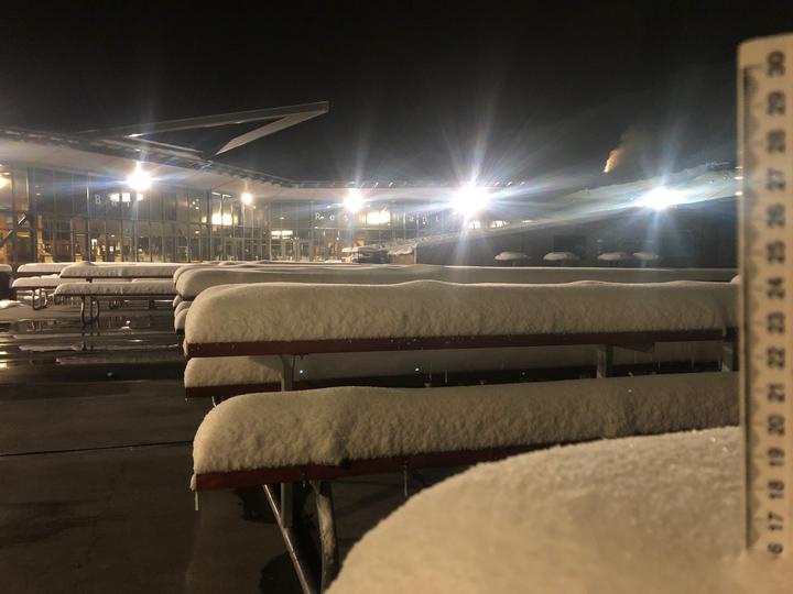 snow piled upon
picnic tables under artificial lights at night