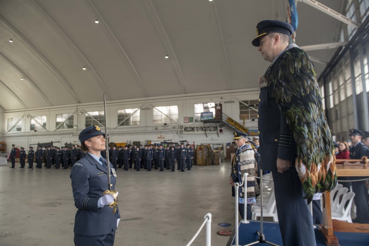 Andy Scott stand on
a platform facing a RNZAF member with a sword below him.
More staff and public are visible in the background 