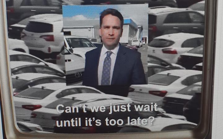 showing simon
bridges in a square, displayed inside a picture of many cars
in a lot. Subtitled 'can’t we just wait until it's too
late?'