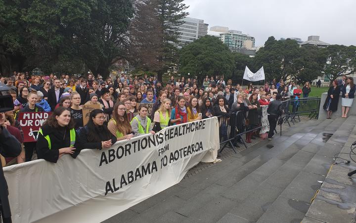 a large crowd at
parliament grounds. A banner draped across the barrier reads
'abortion is healthcare from alabama to aotearoa