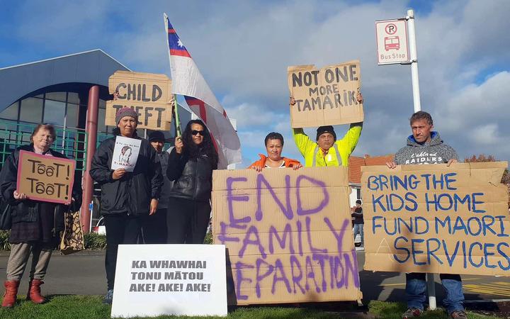 a group of roadside
protestors holding up signs, the largest says 'end family
separation'