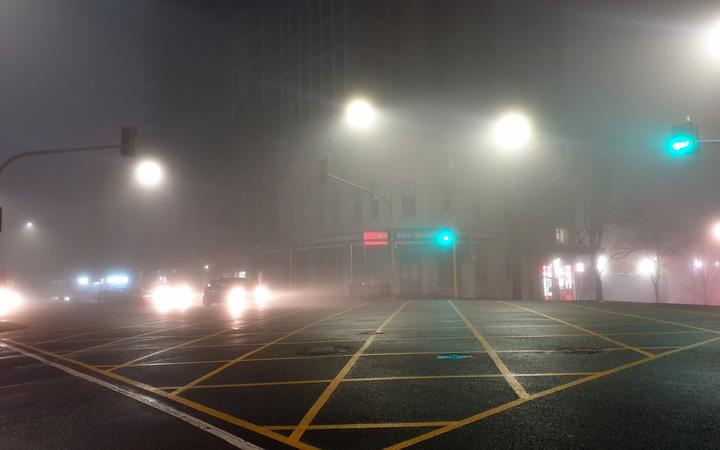 a photo of a city
intersection at night with street and car lights showing
through fog