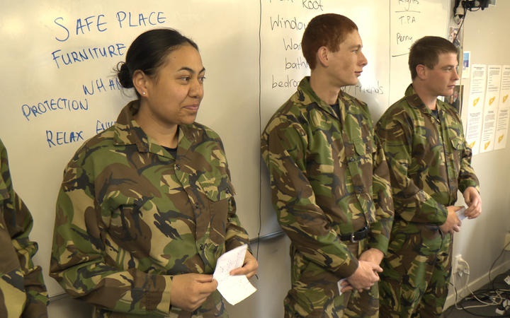 a group of young
people standing against a whiteboard, wearing camo shirt and
pants