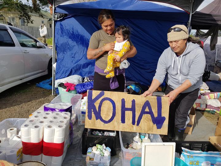 a woman holds a
'koha' sign over boxes of toiletries and other items