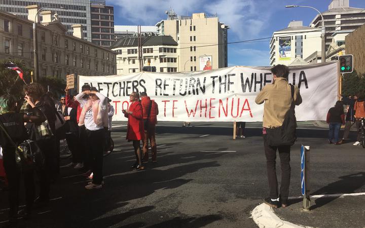 a banner stretch
across the road reads 'Fletchers Reurn The Whenua'