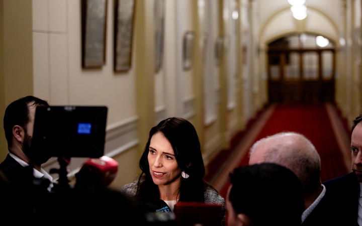 Jacinda Ardern
facing media with a Parliament corridor in the background