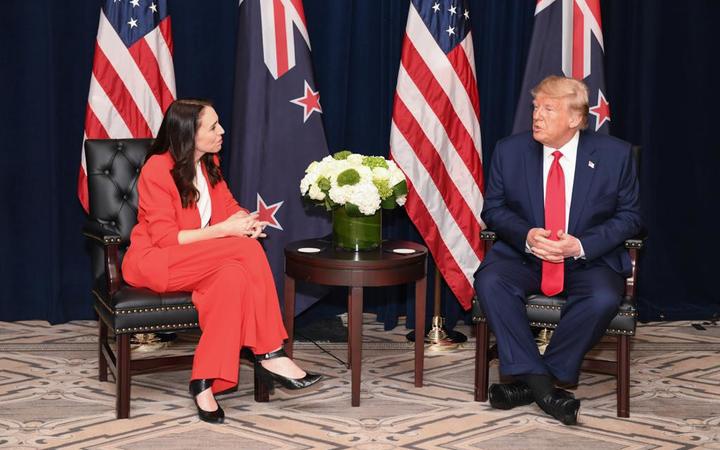 Ardern and Trump
sitting in more or less forward-facing armchairs in front of
US and NZ flags