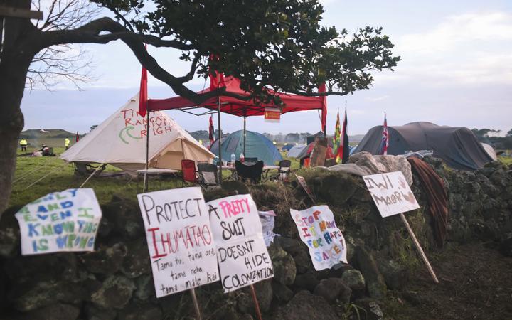 placards and small
banners against a stone fence, with a tree and occupation
tents on the other side