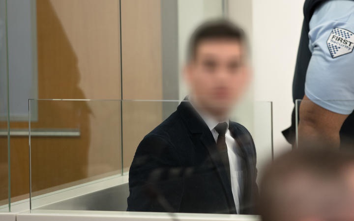 a man sitting in
court, wearing a suit, with the face blurred