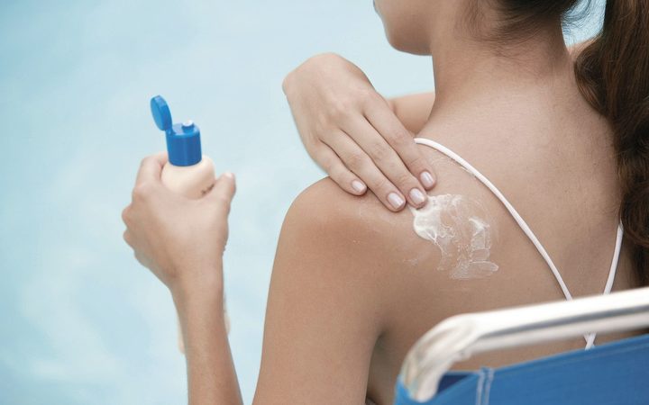 a person in a
swimsuit applying sunscreen to their shoulder